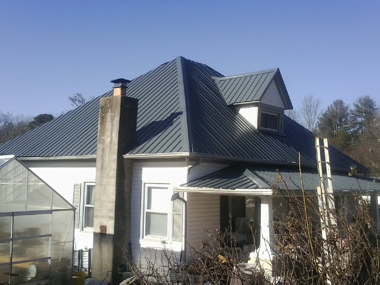 Dark blue standing seam metal roof on a white farmhouse with dormer — Slate & Tile Roof Repair by Roofing Brothers in Blair