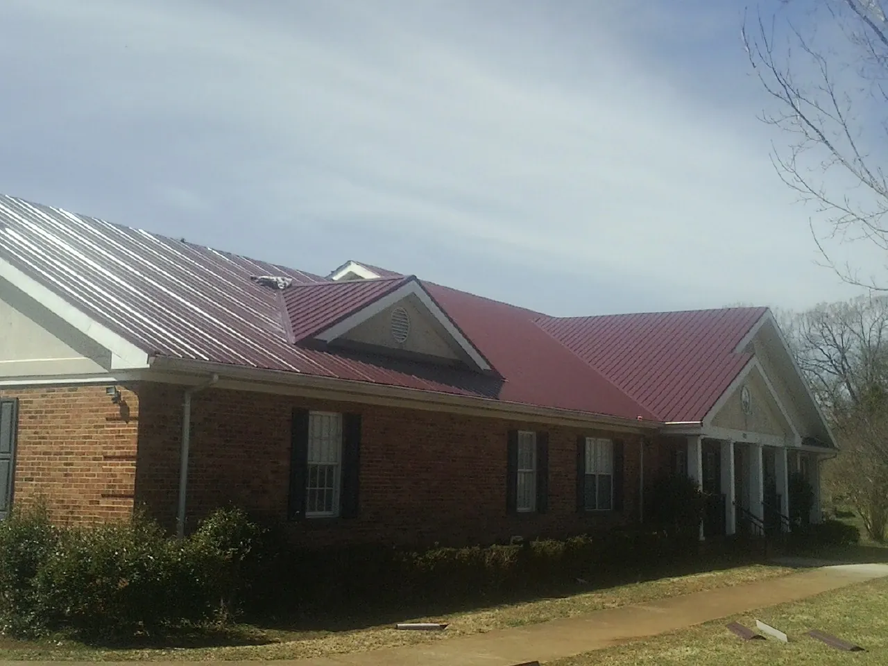 Red metal roof with gabled entries on a long brick building, from a Hail Damage Roof Repair job in Blair