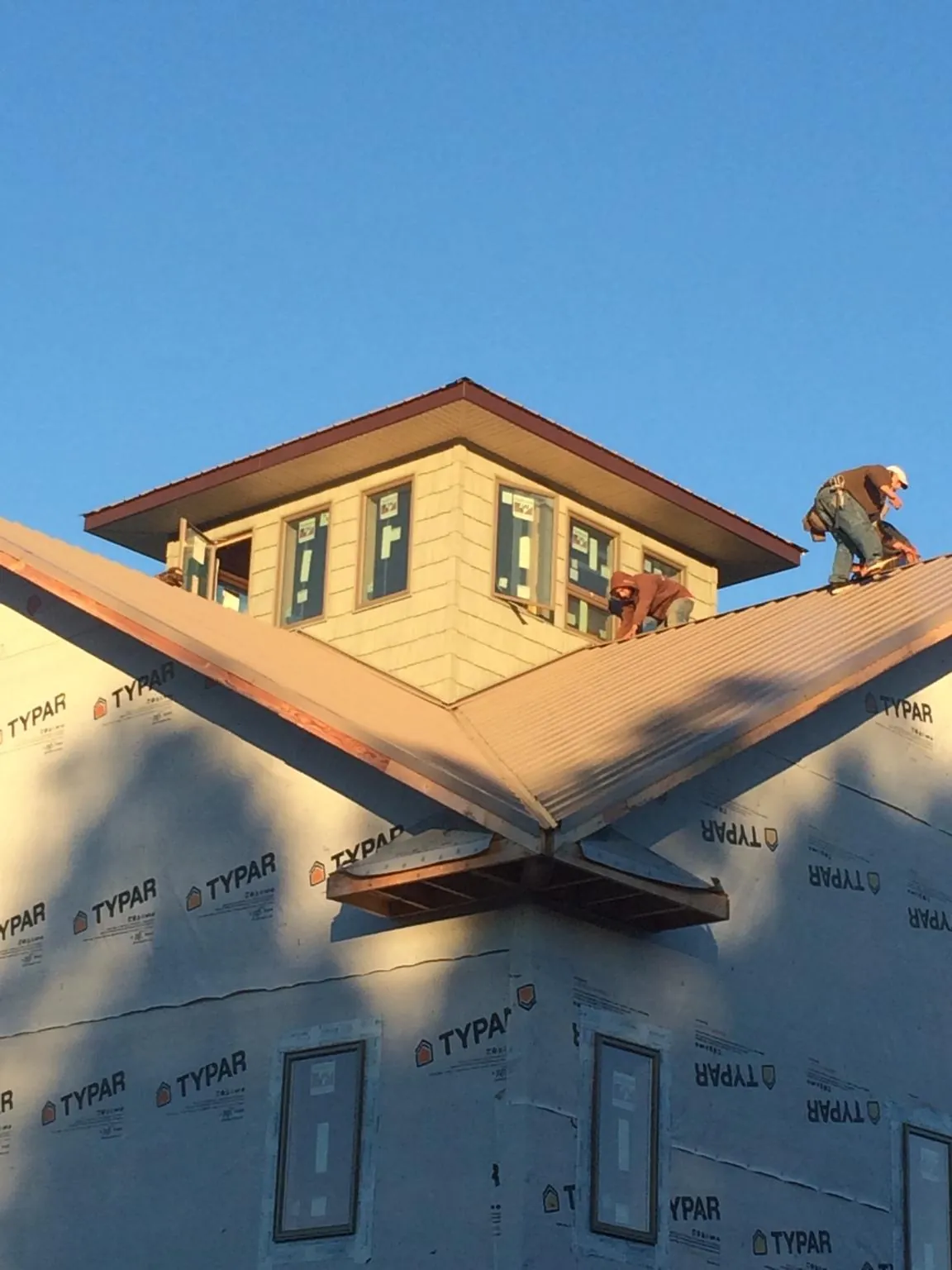 Roofers working around a rooftop cupola on a new metal roof at sunset — Roof Waterproofing in Blair by Roofing Brothers